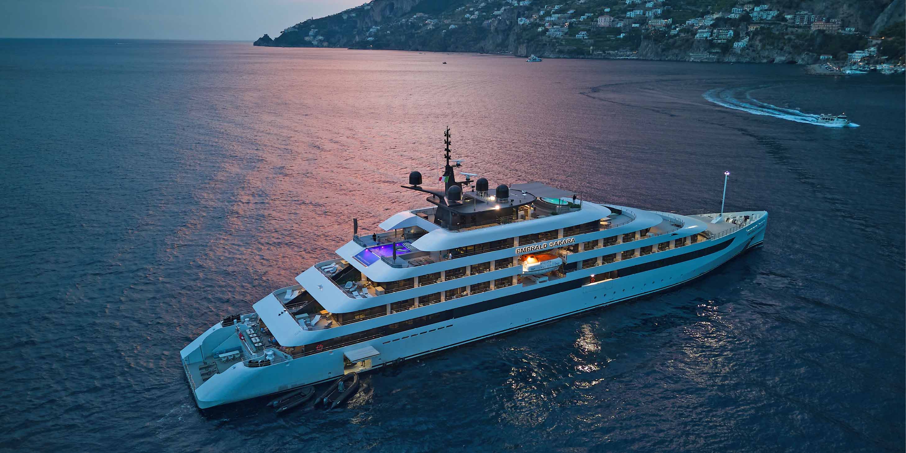 A yacht ship anchored by the Amalfi coast with a pink sunset reflecting from the water