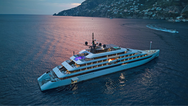 A yacht ship anchored by the Amalfi coast with a pink sunset reflecting from the water