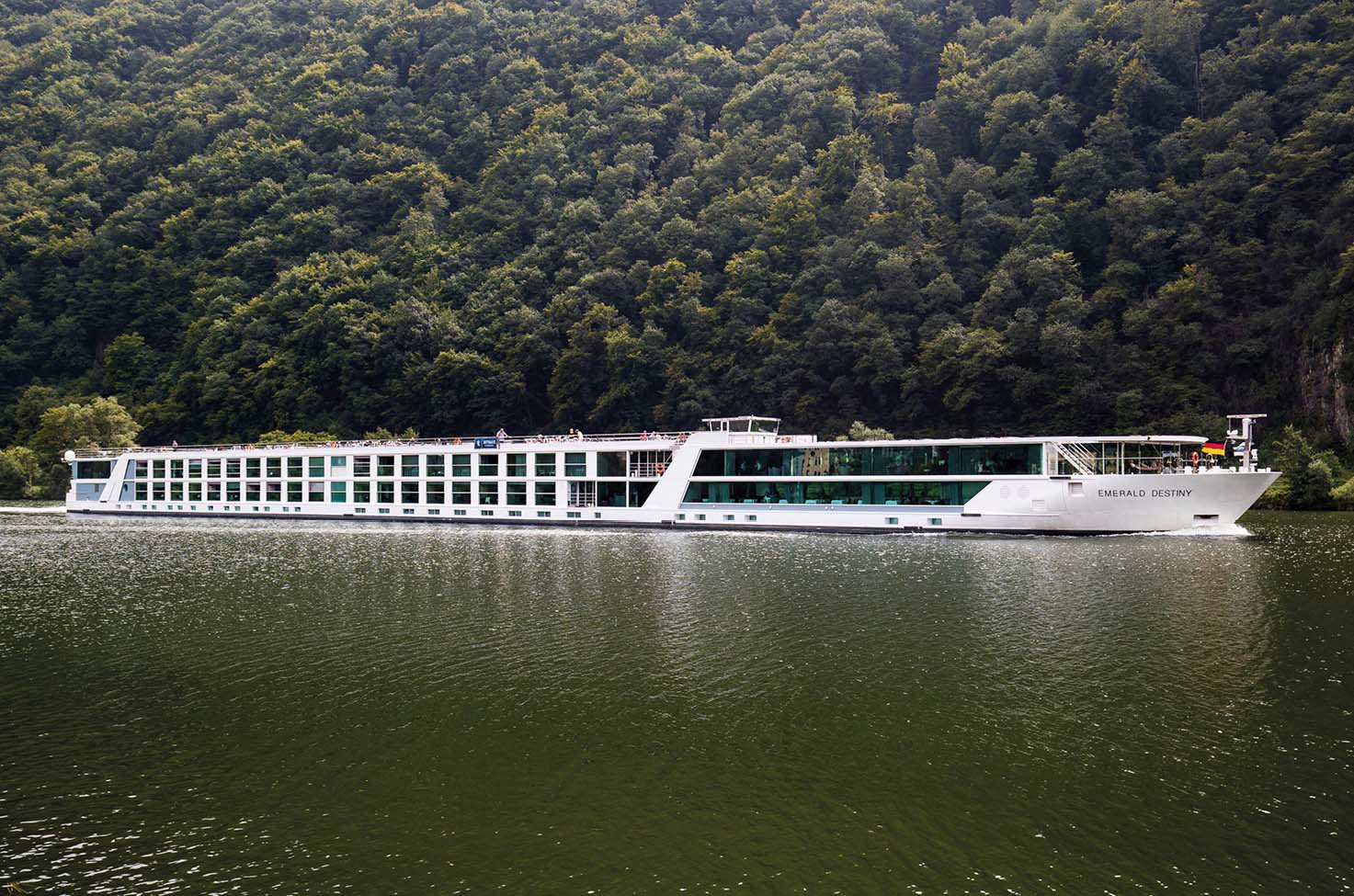 Luxury river cruise ship sailing on calm waters past forestry in Central Europe