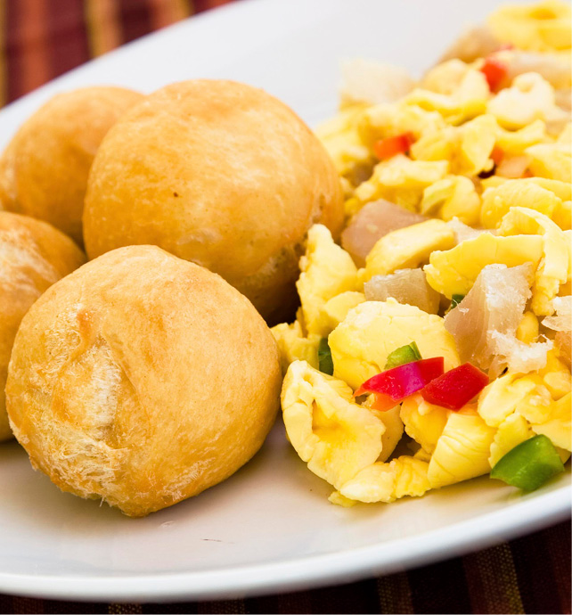 round bread rolls next to a dish of ackee with saltfish