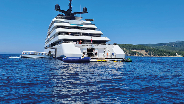 Luxury yacht on the deep blue sea, with guests gathering round the marina toys found near the rear of the yacht. 