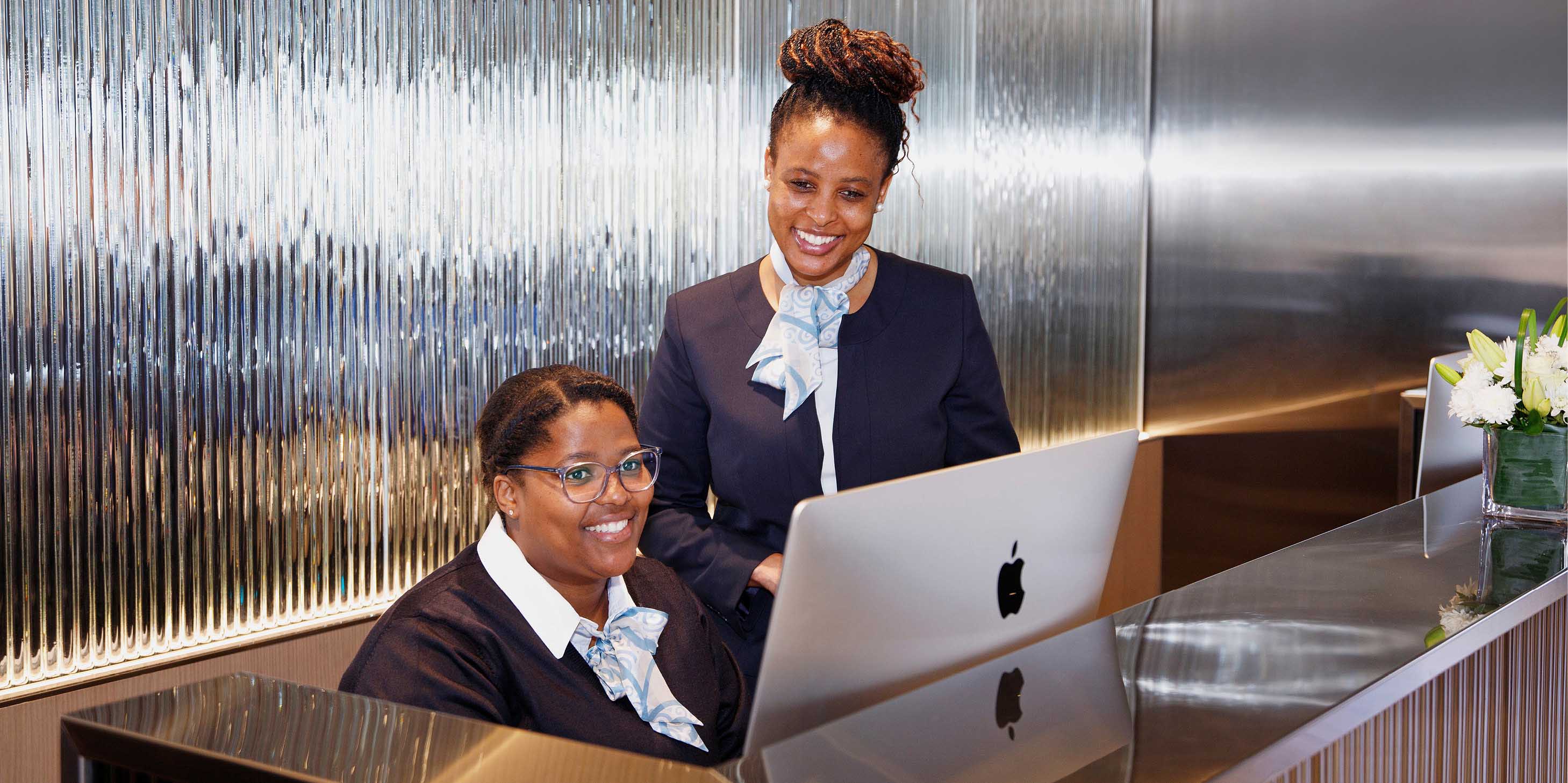 two staff members working behind a computer screen at the reception desk whilst smiling