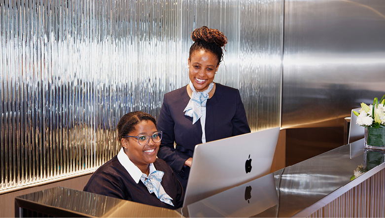 two staff members working behind a computer screen at the reception desk whilst smiling