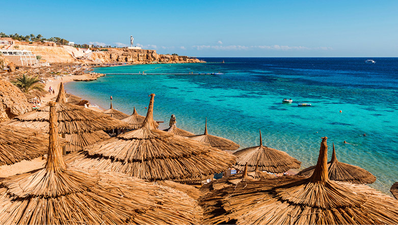 straw thatched parasols lining the curved beachfront on Sharm-el-Sheikh with vibrant blue waters in the background