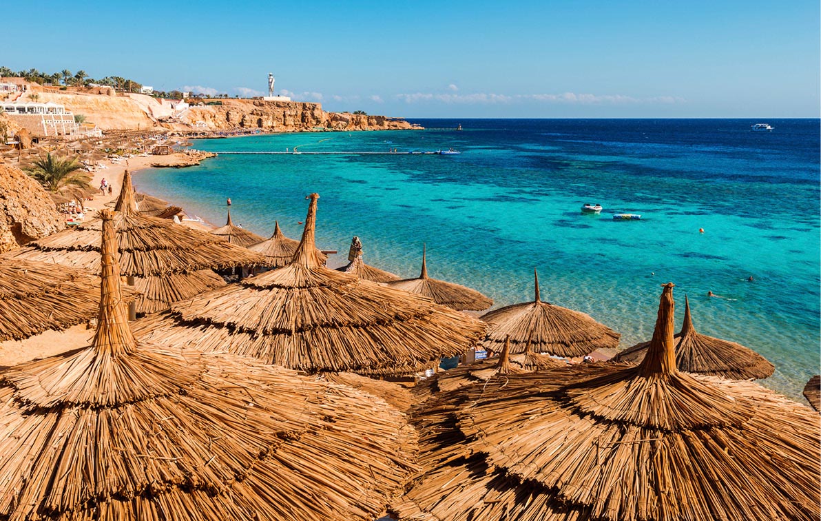beachfront of Sharm el-Sheikh with brown straw-thatched sun umbrellas lining the beach in front of vibrant blue waters