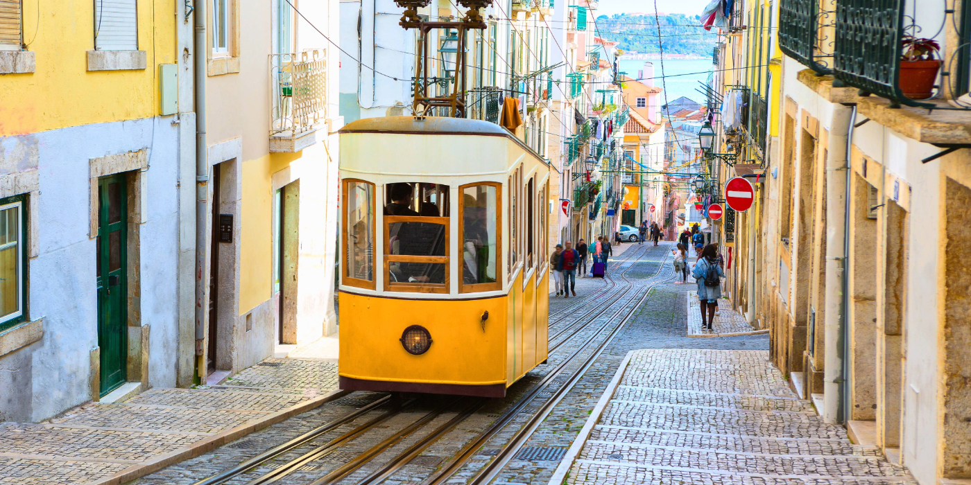 A yellow tram travelling up the streets of Lisbon