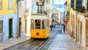 A yellow tram travelling up the streets of Lisbon