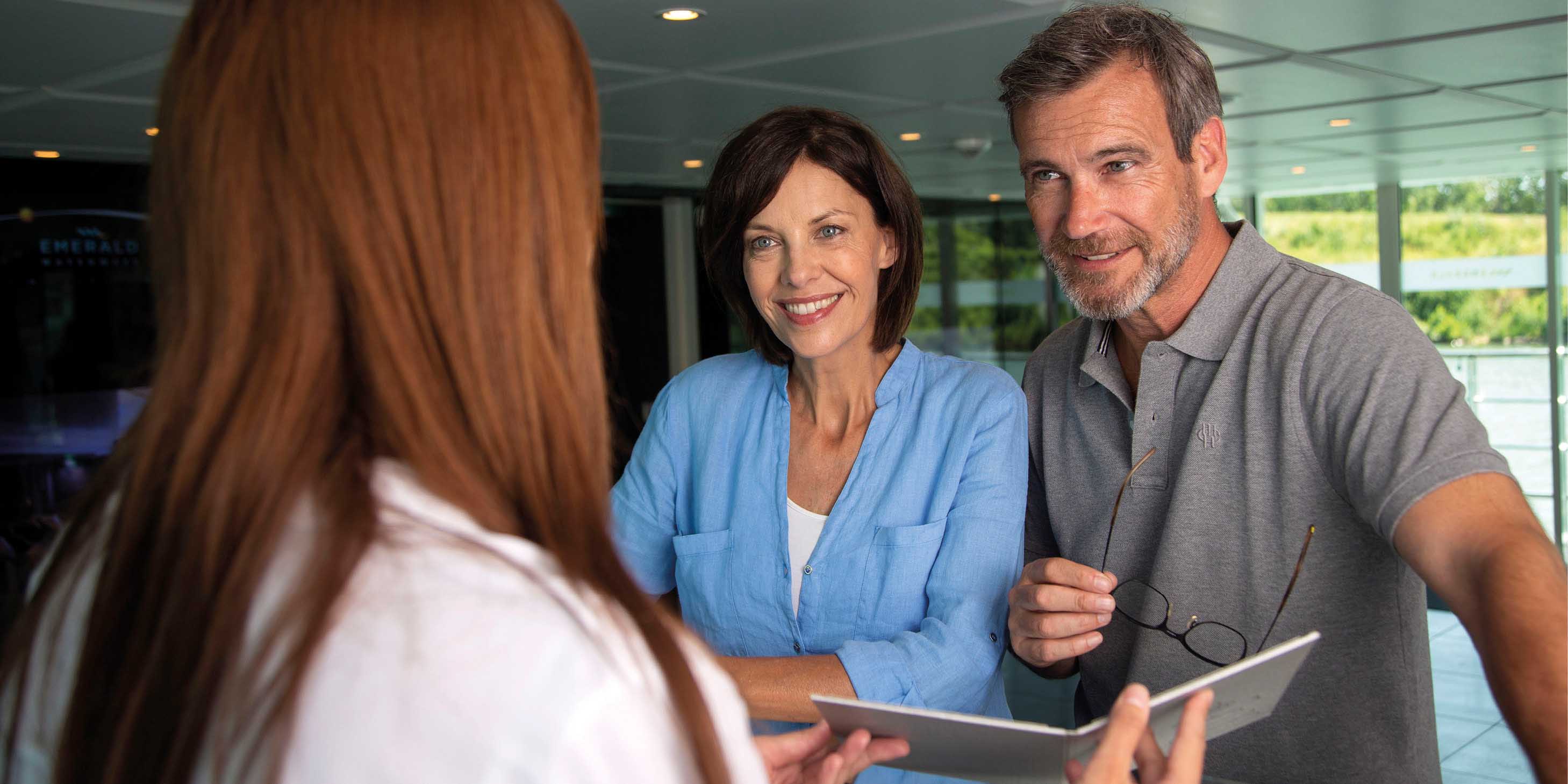 Smiling couple at a reception desk, speaking with the receptionist