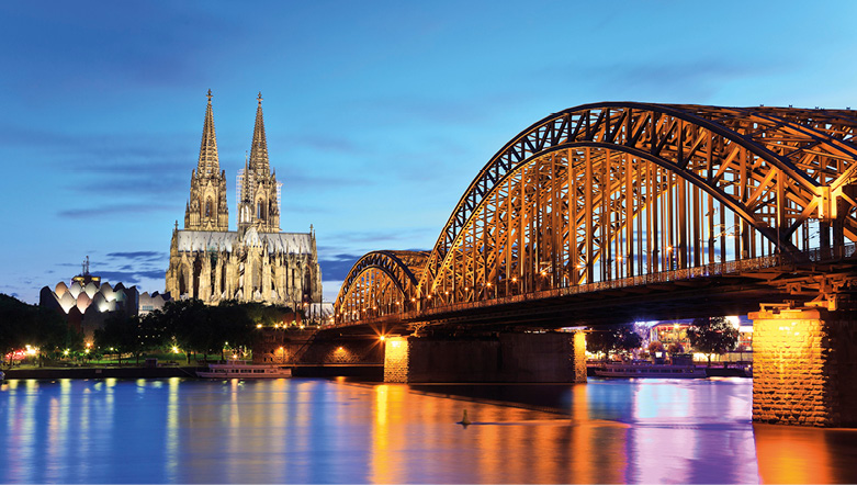 Cologne Cathedral at night with the city glow reflected in the Rhine River and Hohenzollern Bridge