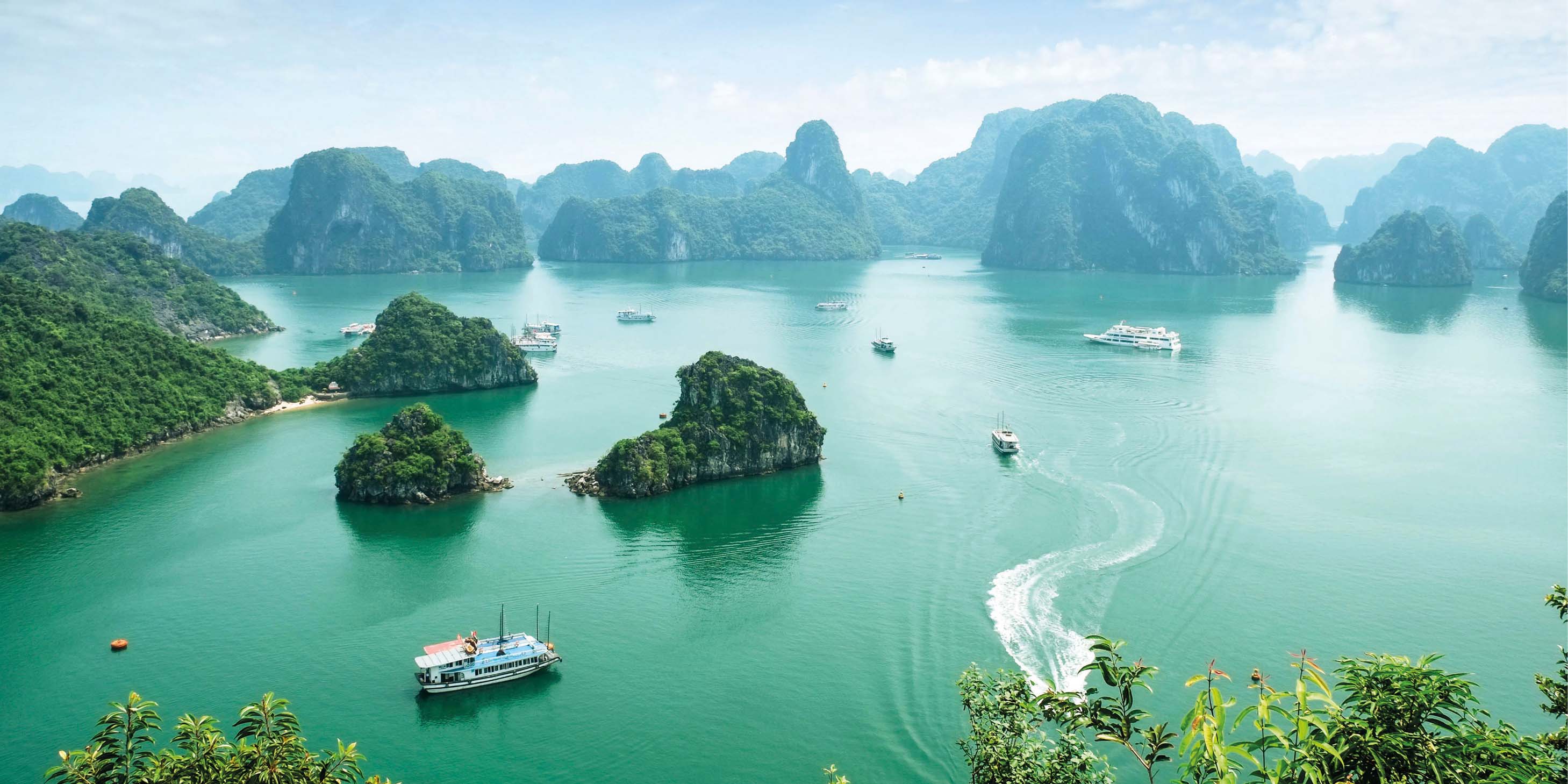 Halong Bay, Vietnam, with fishing boats sailing near the coast, island cliffs with mist in the background