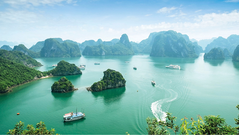 Halong Bay, Vietnam, with fishing boats sailing near the coast, island cliffs with mist in the background