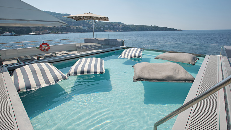 Man swimming in a large infinity-style swimming pool on board a luxury yacht, with stunning views of the sea