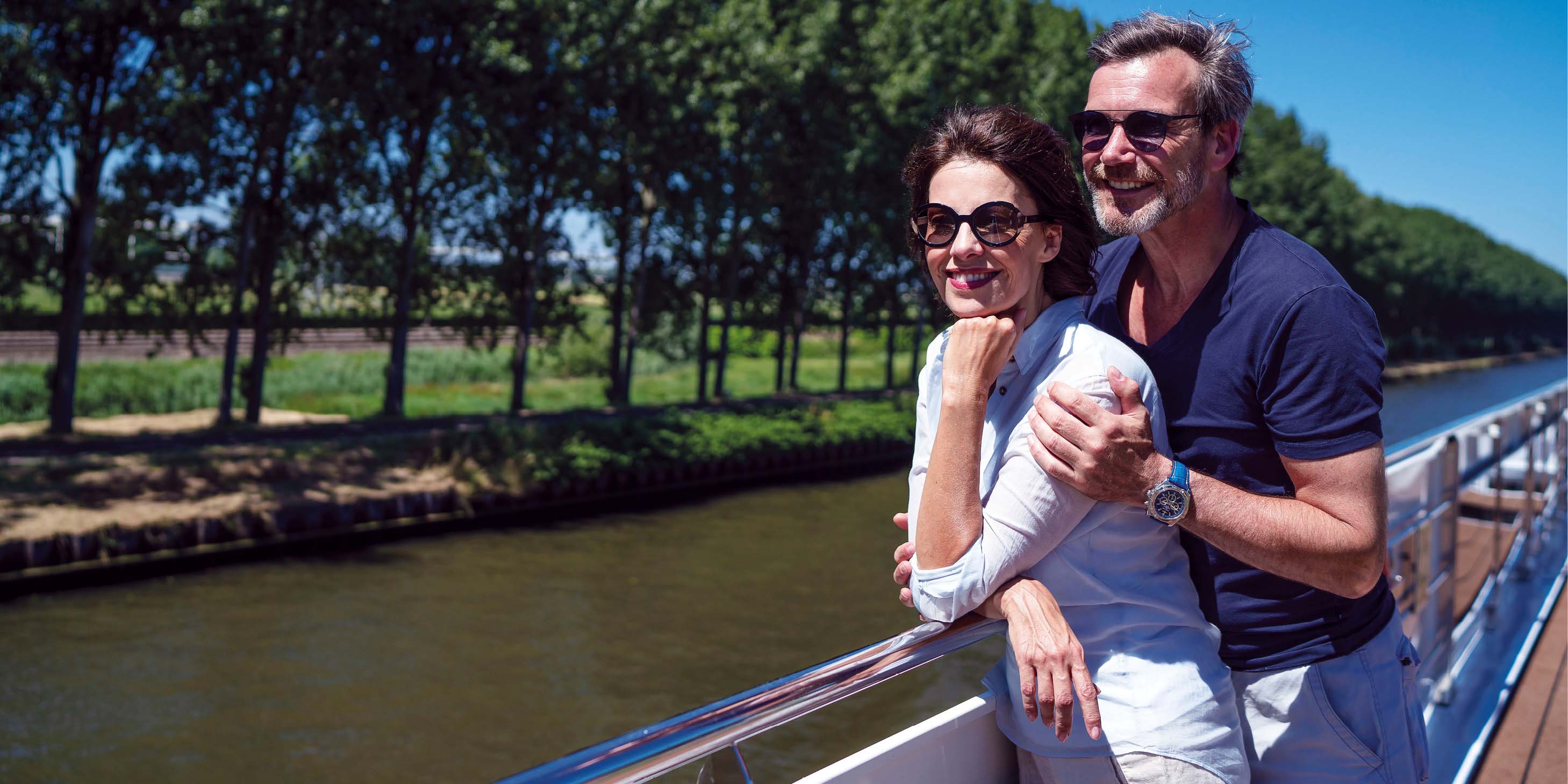 Couple stood on the Sun Deck of a luxury river ship, admiring the passing landscapes