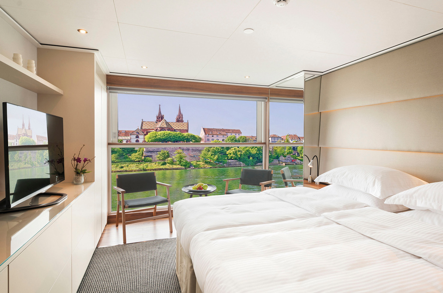 A modern balcony suite with a crispy white queen size bed, tv, and comfortable seating on board an Emerald Cruises river ship sailing through the heart of Europe.