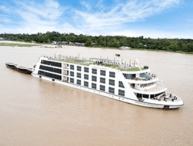 Emerald Harmony cruising along the Mekong River, with the trees along the banks and a blue cloudy sky above