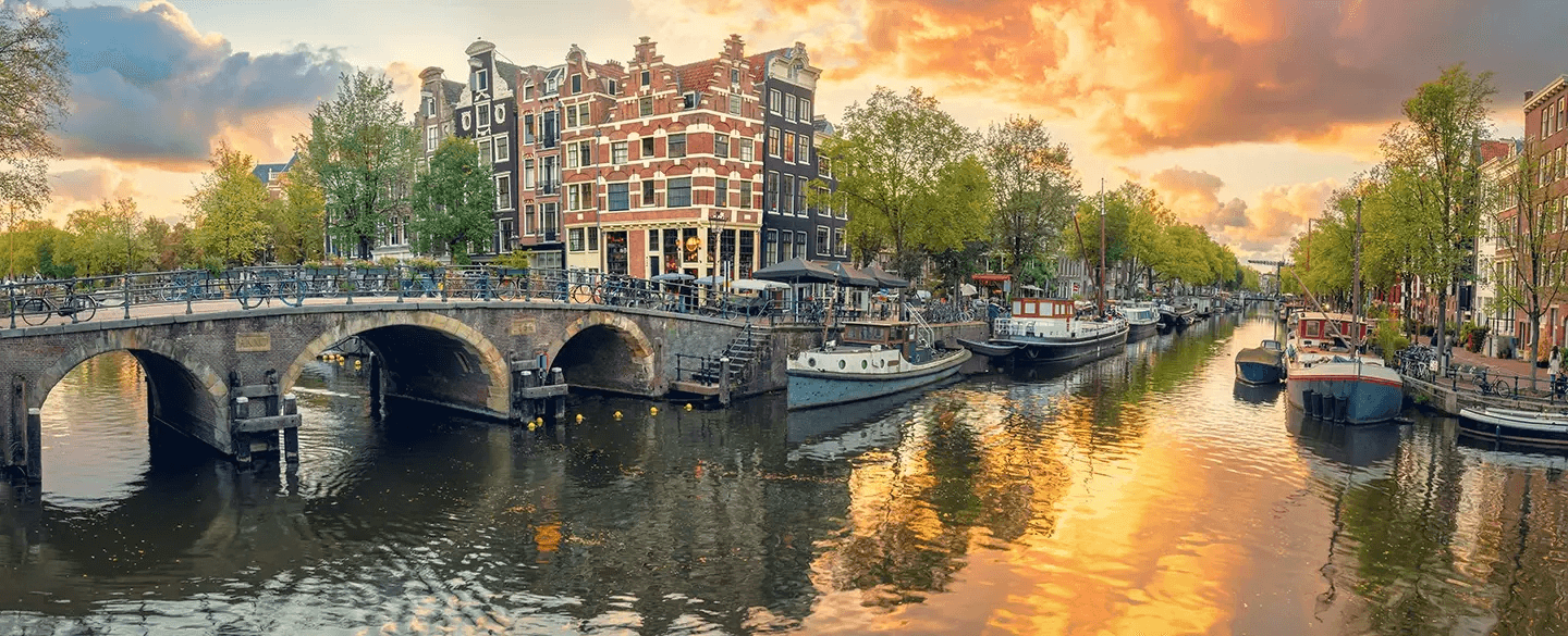 Panoramic shot of Amsterdam at sunset, with traditional canal boats, houses and bridges.