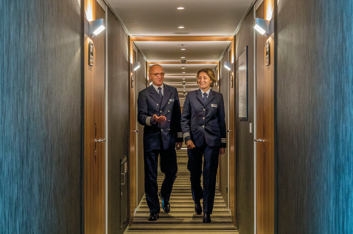 Two cruise ship members walking a corridor and talking to each other