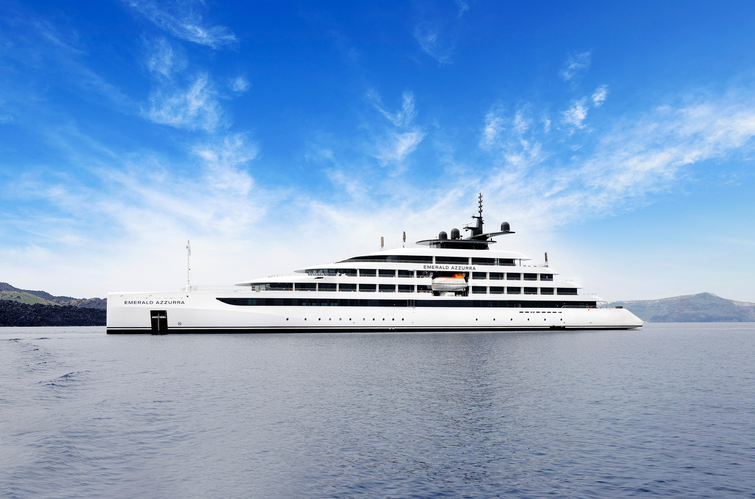 White, small ship luxury yacht sailing on deep blue water under and light cloudy blue sky