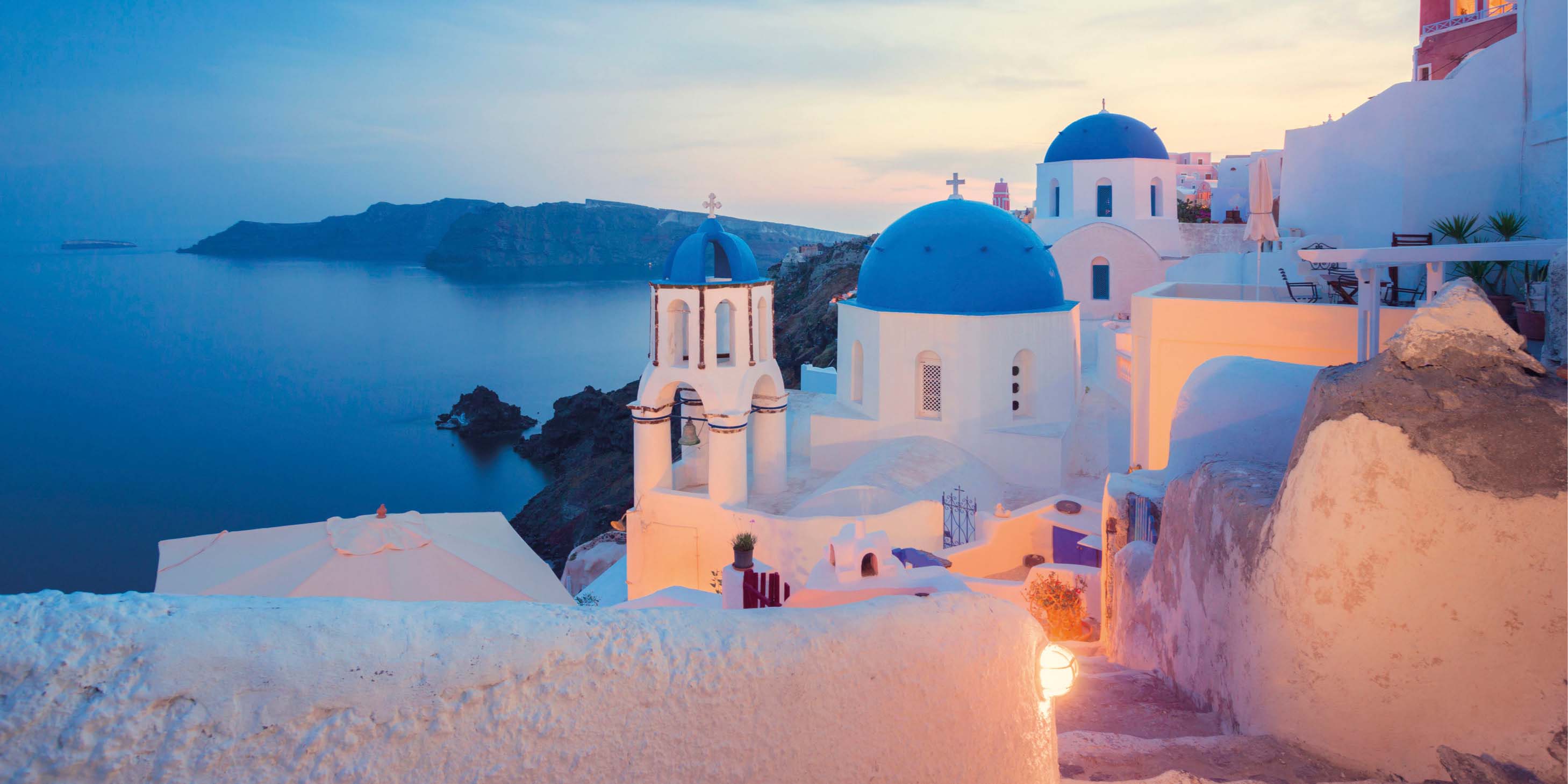 Whitewashed buildings with blue domes at dusk overlooking the tranquil southern Aegean Sea