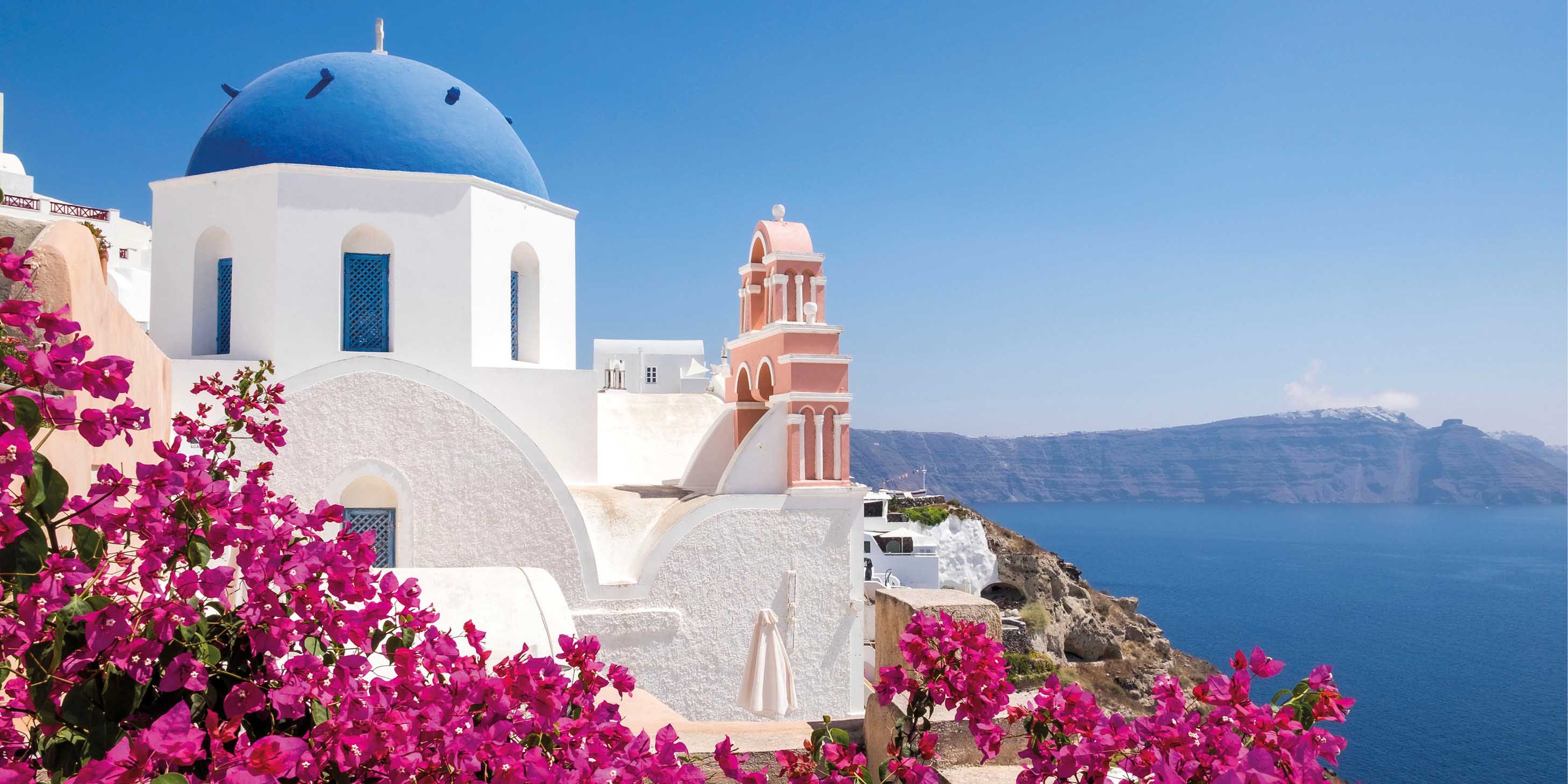 Blue-domed church of Santorini on a bright, sunny day, with the water and sky in background, and flowers in foreground    