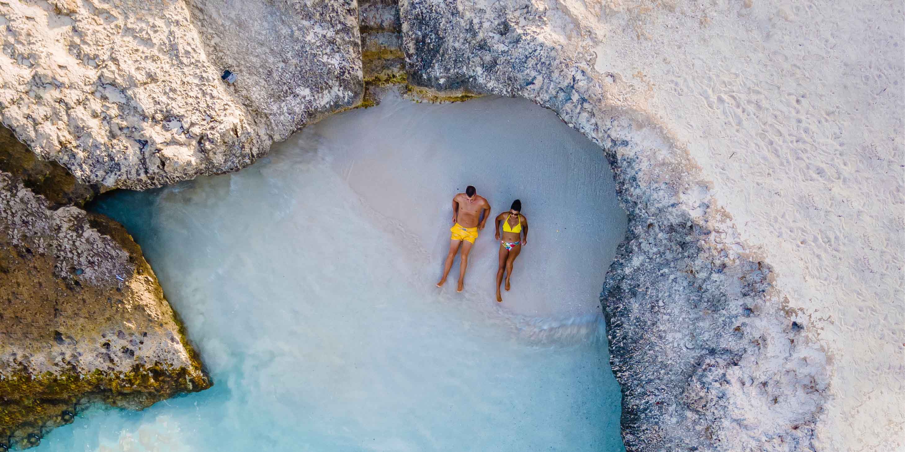 Couple relaxing on a secluded white sandy beach in the Caribbean overlooking crystal-clear azure waters