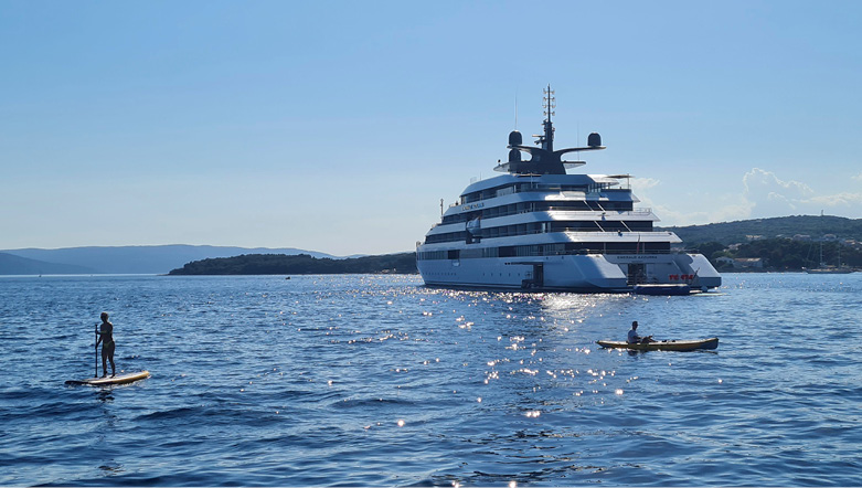 People paddleboarding and kayaking in the calm sea next to an Emerald Cruises luxury yacht